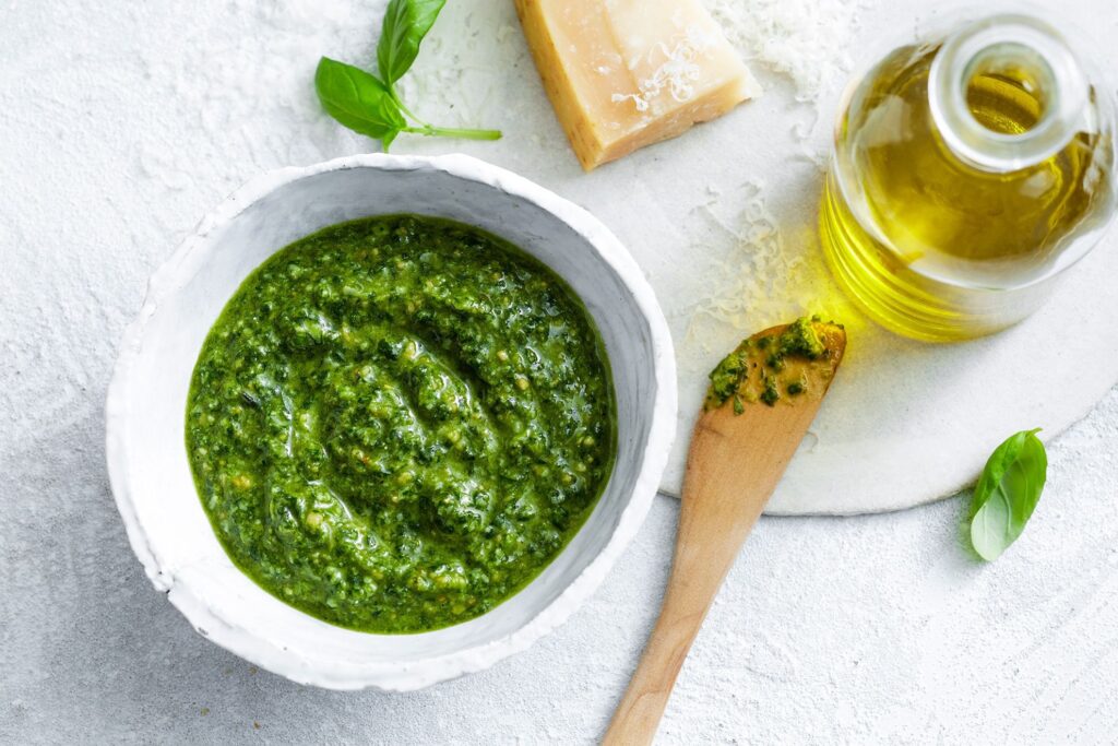 Homemade basil pesto sauce being poured over pasta